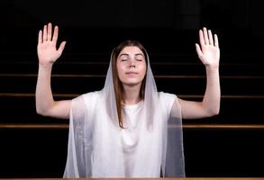 A young modest girl with a handkerchief on her head is sitting in church and praying photo