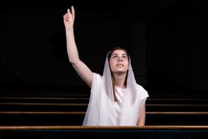 A young modest girl with a handkerchief on her head is sitting in church and praying photo