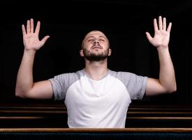 A Christian man in white shirt is sitting with his hands up and praying with humble heart in the church photo