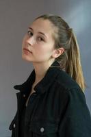 Three quarters shot or semi profile portrait of a pretty teenage girl with ponytail hair posing looking at the camera over a grey background photo