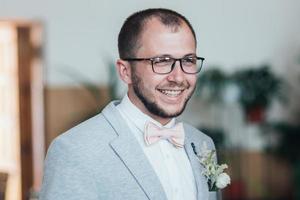 Wedding photo of emotions of a bearded groom with glasses in a gray jacket and rustic style