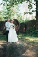 Foto de boda de la novia y el novio en un color rosa grisáceo en la naturaleza en el bosque y las rocas