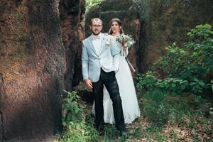 Bride and groom on wedding day hugging standing near a rock or a large stone photo