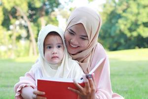 Madre musulmana enseña a su hija a leer felizmente el Corán en el parque en verano.