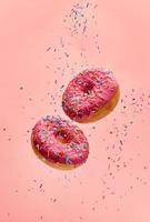 Dos donas levitando con chispitas de azúcar sobre un fondo de color rosa foto