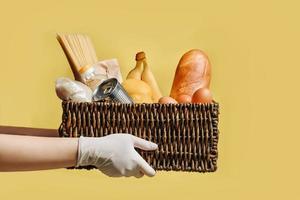 Wicker basket with a set of products in the hands in protective gloves isolated on a yellow background photo