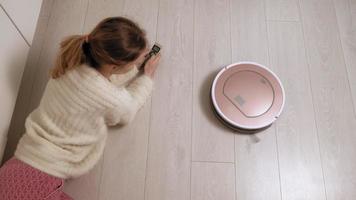 A young woman controls a robot with a vacuum cleaner