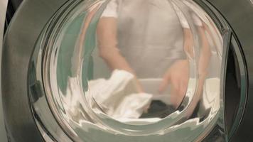 uma mulher separa a roupa antes de lavar, vista de dentro da máquina de lavar video