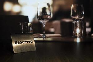 A metal plaque with the words reserved stands on the left on a wooden table in a restaurant with a candle and glasses in the background photo