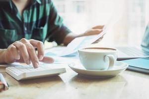 The accountant is pressing the calculator to calculating check the accuracy of the investment budget with using computer laptop and document data to analysis photo