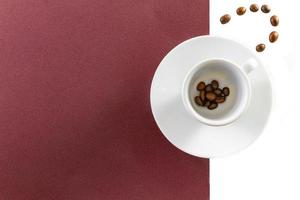 Vista superior de una taza de café y granos de café sobre fondo blanco y marrón