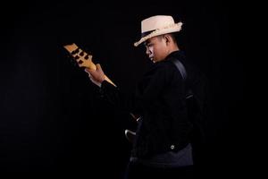 Young man in black leather jacket with electric guitar against black background in studio photo