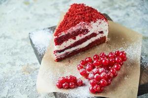 Red velvet cake and a bunch of red currants on a wooden board