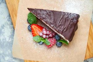 A slice of chocolate cake decorated with berries on a wooden board photo