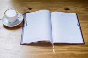 Notebook with cup of coffee on wooden desk photo