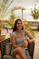 Mujer joven bebiendo jugo de naranja en el café de la calle foto