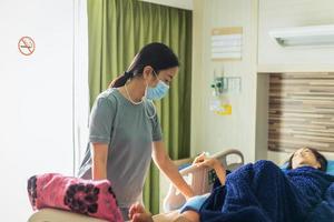 Hija en máscara médica visitando a su madre acostada en la cama en la sala del hospital