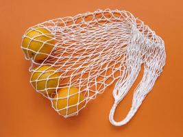 White string cotton eco bag with oranges on orange background Monochrome simple flat lay Ecology zero waste concept Stock photo