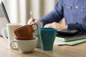 used coffee cups on the office desk and a man working hard drink several cups of coffee to stay refresh in the background photo