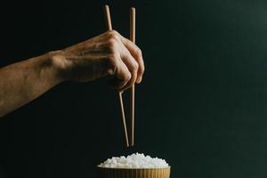 Hands grabbing japanese chopsticks over a bowl of rice photo