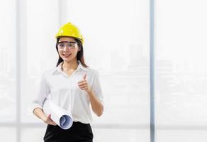 Portrait of a beautiful architect wearing a yellow helmet at work and a document on a construction site photo