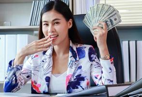 Successful asian business woman holds a dollar and smiles happily photo