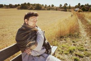 Un hombre joven con una bufanda caliente disfrutando en la calma del sol de otoño de la mañana en un campo amarillo con la luz de fondo del cielo azul foto