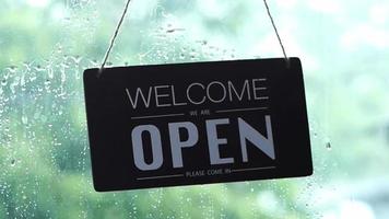 un letrero abierto que cuelga en la puerta principal del restaurante balanceándose en un día lluvioso video