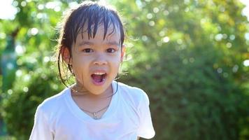 felice bambina bambino divertirsi a giocare con la pioggia alla luce del sole di sera bambina cattura gocce d'acqua sotto la pioggia doccia in cortile video