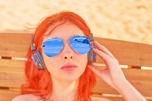 Bella mujer con gafas de sol escuchando música en la playa foto