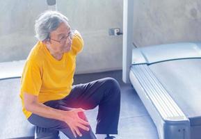 Hombre asiático con gafas se sienta en el suelo debido al dolor de rodilla por hacer ejercicio en el gimnasio foto