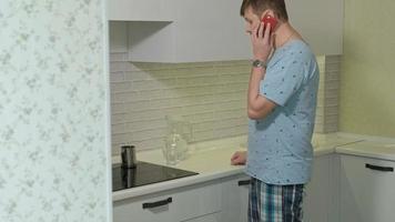 Un hombre en pijama bebiendo agua en la cocina por la mañana. video