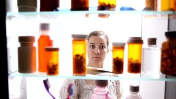 Woman looking for pills in medicine cabinet video