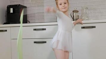 uma menina feliz em um maiô branco de ginástica treina danças com uma fita para ginástica rítmica, salta e realiza exercícios profissionais video