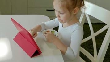 petite fille mange et joue à l'aide d'une tablette surfer sur le web video