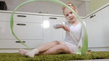 A happy little girl in a white gymnastic swimsuit trains dances with a ribbon for rhythmic gymnastics jumps and performing professional exercises