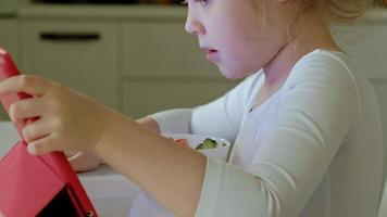 petite fille mange et joue à l'aide d'une tablette surfer sur le web video