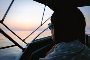 Woman sits in front of the boat and looks to blue black sea horizon after the sunset photo