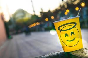 Vaso de papel desechable amarillo y cara sonriente en él de pie en el lateral del estante con la mezquita azul en el fondo foto