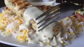 A fork cutting chicken kebab with white sauce on it close up photography