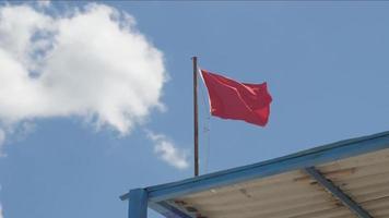 Drapeau d'avertissement rouge flottant au vent sur ciel bleu video