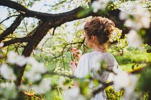 Novia joven con cabello rubio posando en el fondo del huerto de primavera