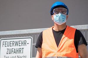 Trabajador de la construcción vistiendo casco azul, chaleco reflectante y mascarilla quirúrgica protectora foto