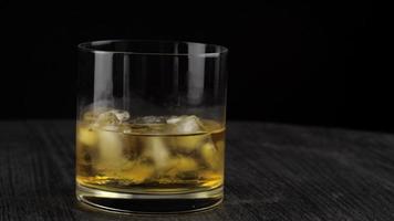 Whiskey is poured into a glass with ice dark room video