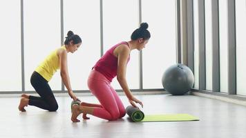 duas mulheres asiáticas se preparam para se exercitar, relaxar ou rolar um tapete de ioga video