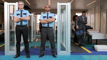 Zwei Sicherheitspersonal des Flughafens stehen vor einem Metalldetektor video
