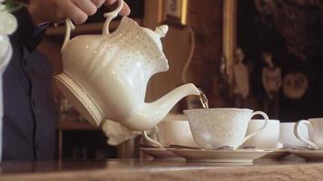 um homem derrama o chá de uma chaleira em uma xícara branca sobre uma mesa de madeira video
