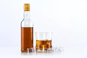 Vaso de whisky con cubitos de hielo y botella sobre fondo blanco. foto
