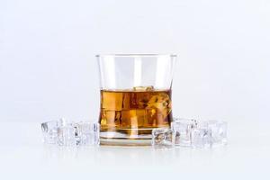 Glass of whiskey with ice cubes on white background