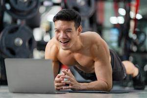 Online training  Sport man training doing push ups exercise with laptop in fitness gym photo